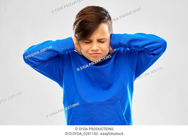 stressed boy in blue sweater closing ears by hands