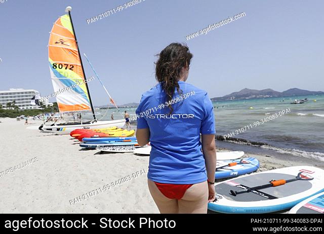 11 July 2021, Spain, -: Anna, the teacher of a water sports school, prepares surfboards for windsurfing on the beach of Playa de Muro in the north of Mallorca