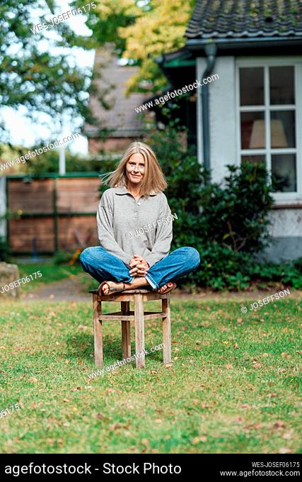 Smiling woman sitting cross-legged on stool at backyard
