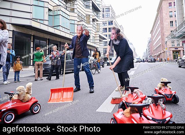 03 July 2023, Berlin: A demonstrator with a ""Kai Wegner mask"" and a demonstrator with a ""Manja Schreiner mask"" symbolically sweep the Bobby-Cars out of the...