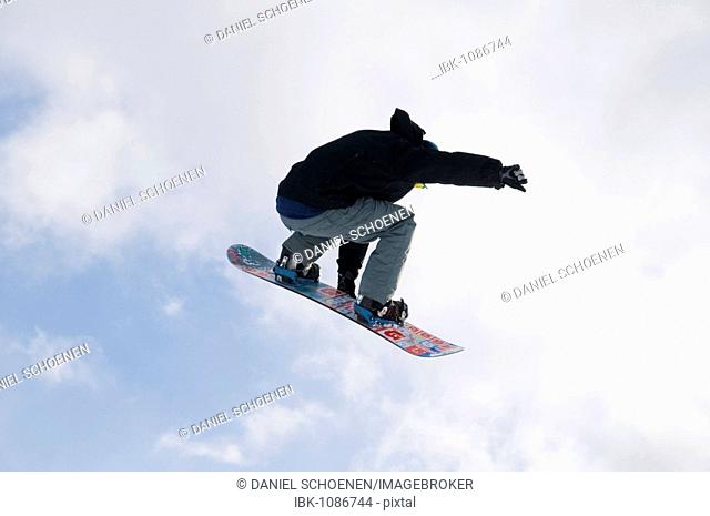 Snowboarder jumping in front of a blue sky with clouds and the sun