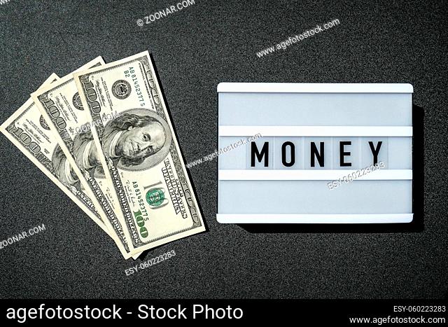 Lightbox board with the word MONEY in black letters around Us dollars banknotes. Finance background. Business, financial success and making money concept
