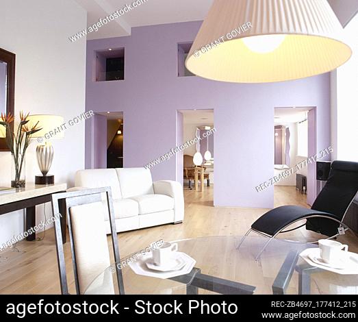 Glass top dining table, sofa, wood floor, and a lilac accent wall with doorways to an adjacent room