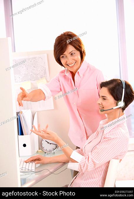 Smiling coworkers discussing work in office, supervisor pointing at customer care operator computer screen