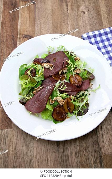 Sliced saddle of venison on salad leaves with plums and walnuts