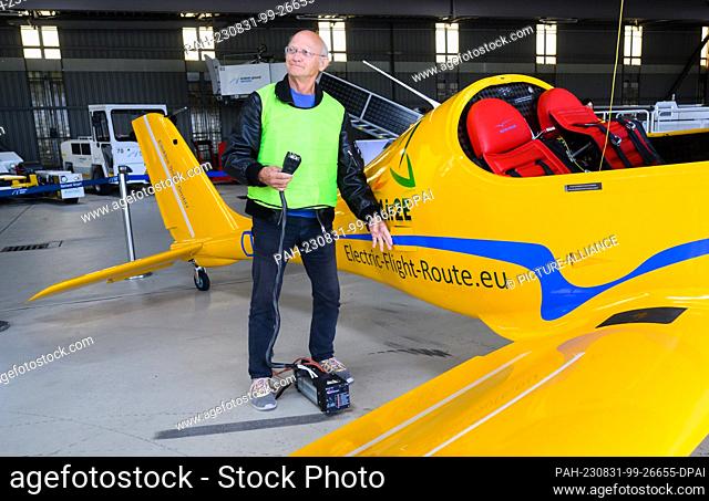 31 August 2023, Lower Saxony, Hanover: Test pilot Uwe Nortmann stands with a voltage converter in front of the ""Elektra Trainer"" e-airplane at Hannover...