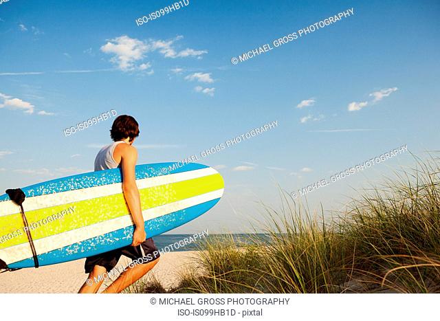 Teenager carrying surfboards to beach beside dunes
