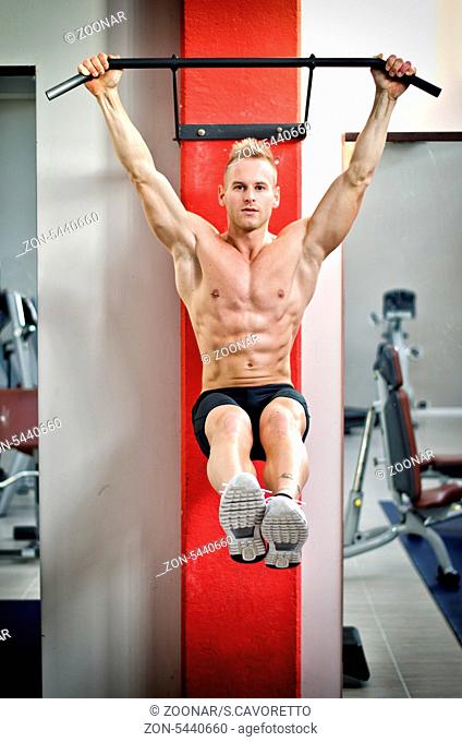 Blond, attractive young man hanging from gym equipment, looking at camera