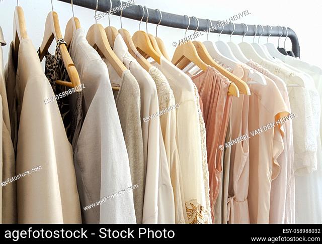 Stylish womans clothes hanging on a rack natural colors, trending concept, pastel colors in white room modern design closeup storage