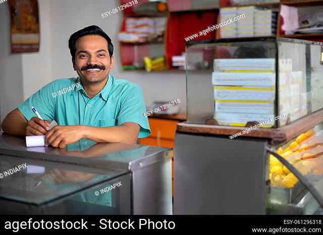 Portrait of Sweet shop owner looking at camera with smile while maintaining accounts at counter
