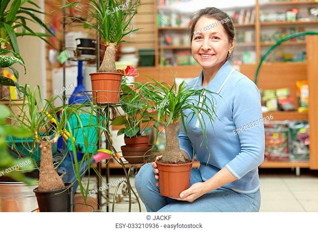 Happy mature woman with Nolina plant in flower store