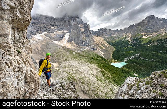 Young man, mountaineer on a fixed rope route, Via Ferrata Vandelli, view of Lago di Sorapis, Sorapiss circuit, mountains with low clouds, Dolomites, Belluno