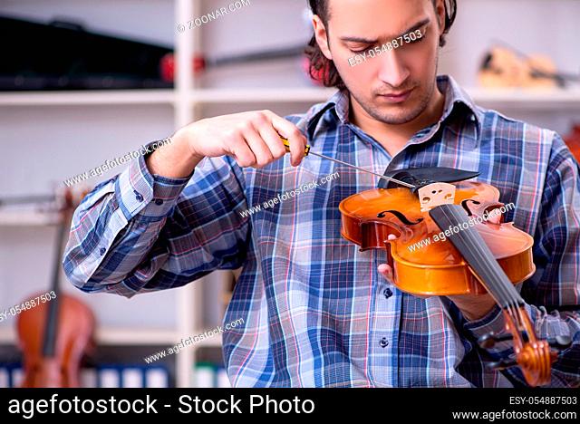Young handsome repairman repairing violin