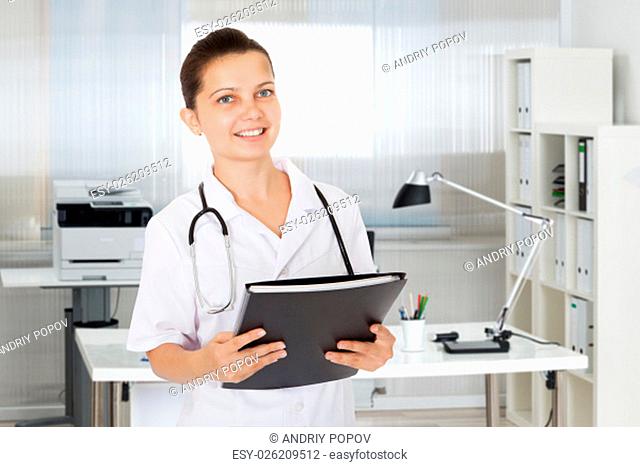 Portrait of happy female doctor holding folder over white background