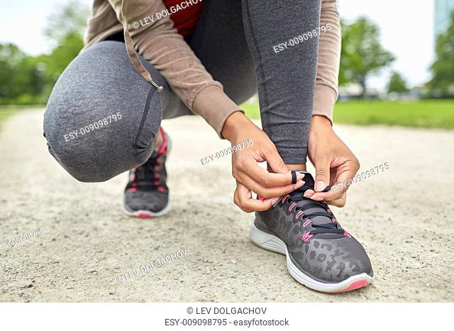 sport, fitness, people and lifestyle concept - close up of woman tying shoelaces outdoors