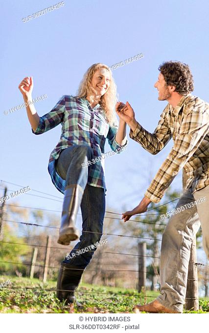 Couple climbing over wire fence outdoors