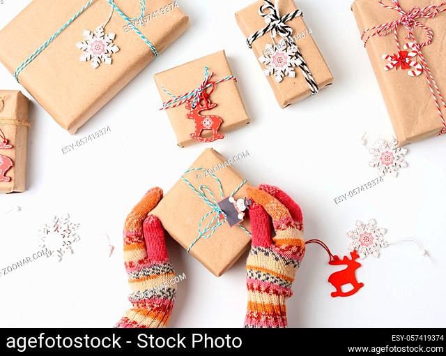female hands in knitted mittens hold a box wrapped in brown paper and tied with a rope on a white background, top view