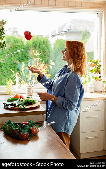 Woman in kitchen throwing fresh red pepper
