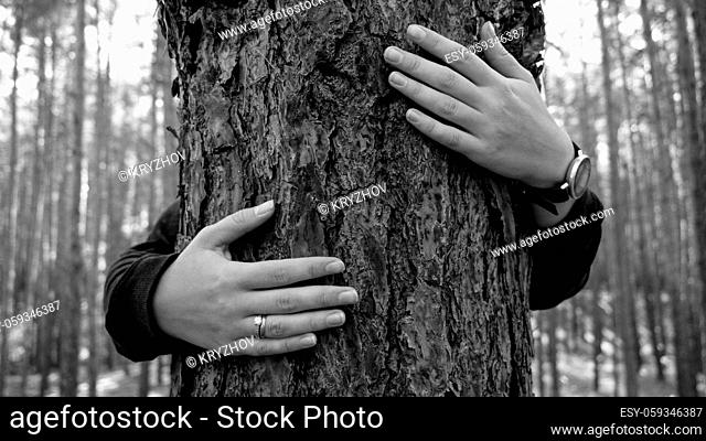 Black and white iamg eof young woman embracin gbig old tree in forest. Concept of love, ecology protection and harmony with nature
