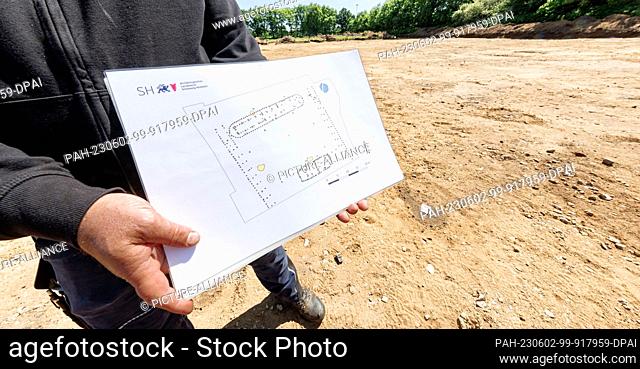 02 June 2023, Schleswig-Holstein, Kropp: The excavation director shows a site plan of houses on an excavation area, which could be created according to the...