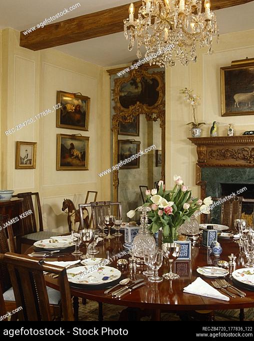 Country dining room with cream walls, fireplace and round polished table set for dinner