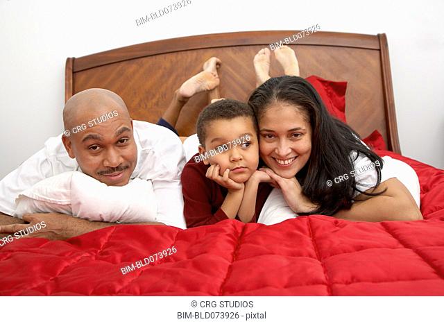 Mixed race boy lounging on bed with parents