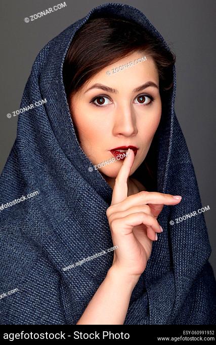 Beauty portrait of brunette woman dressed in dark blue scarf. Female portrait from a three-quarter angle on black background