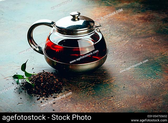 Glass transparent teapot and two glass cups with black tea on a dark table