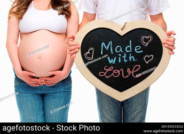 Young pregnant couple holding Made with love chalk board. Isolated over white background