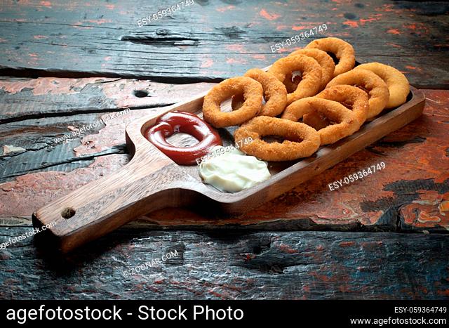 Fried onion rings with ketchup and mayonnaise isolated on rustic wooden table