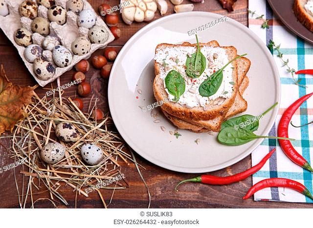 Sandwich with soft cheese and spinach surrounded composition of quail eggs red pepper and walnuts