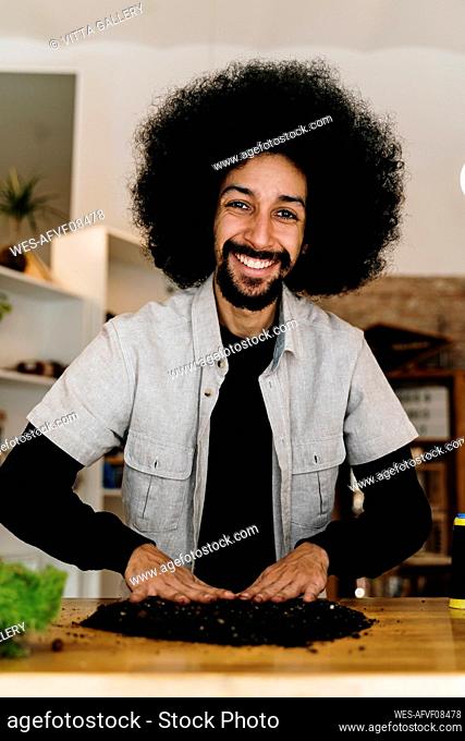 Smiling Afro man making kokedama plant on table at home