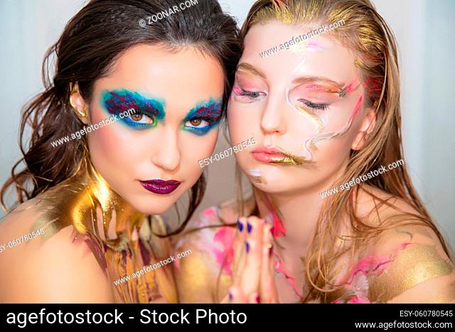 Two nice young women with creative make-up on the face posing in the studio