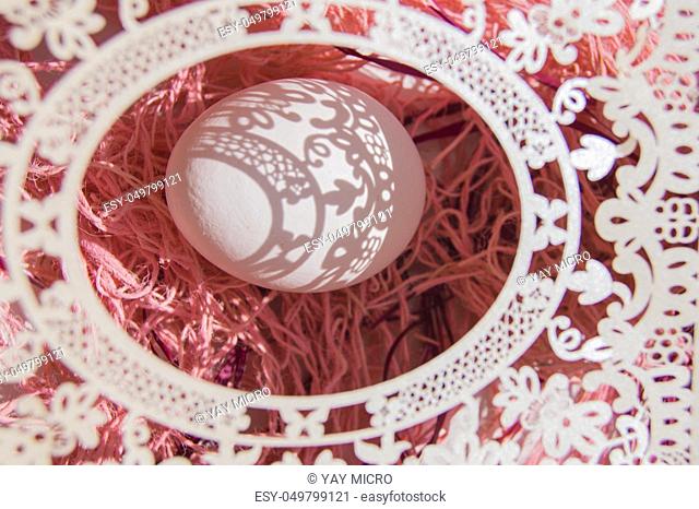 Easter card with egg and white openwork oval frame on coral background, Bright sunlight creates beautiful shadows on white egg, copyspace, top view