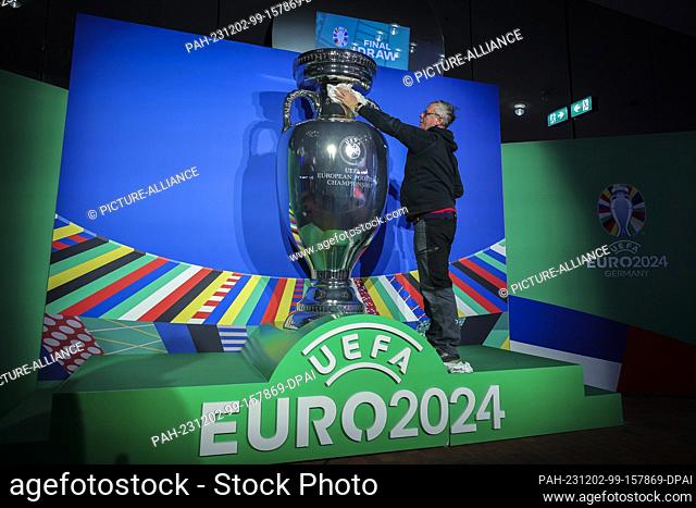 02 December 2023, Hamburg: Soccer: European Championship, draw - preliminary round in Hamburg, Elbphilharmonie. A man cleans an oversized trophy on the plaza...