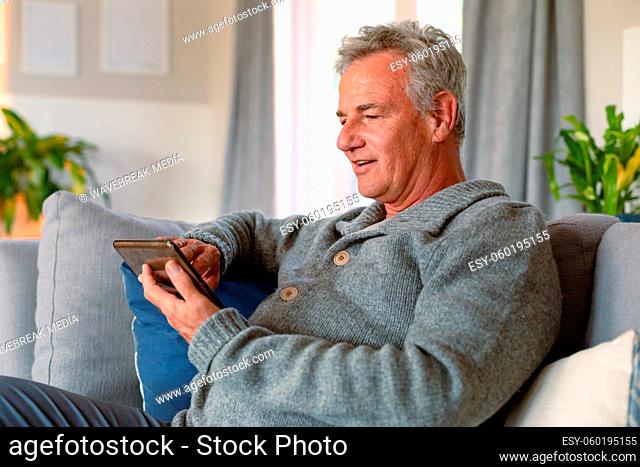 Happy caucasian senior man sitting on sofa and using tablet