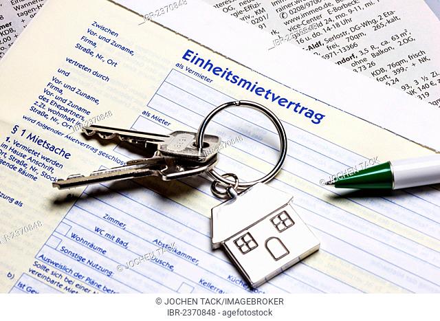 Two keys with a metal key tag shaped like a house lying on a German rental agreement, symbolic image for home, real estate, house purchase