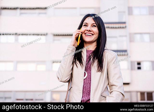 Smiling woman with long hair looking away while talking on mobile phone