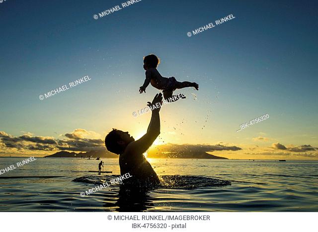 Father playing with his little baby in the water at sunset, Papeete, Tahiti