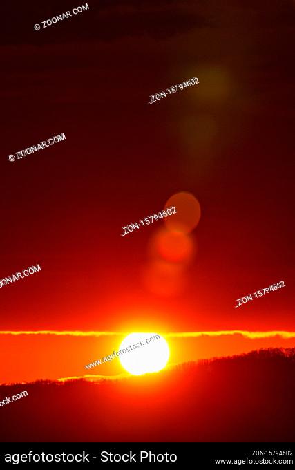 Rising of the sun in mountains, red-orange sun disk rises from tops of mountain range. Beautiful natural lens flare in orange sky, sunbeam light leaks