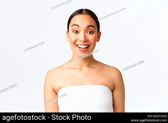 Excited and upbeat smiling asian woman in towel looking intrigued at camera, saying wow, hear about spa salon discounts, special offer on bathroom and skincare...