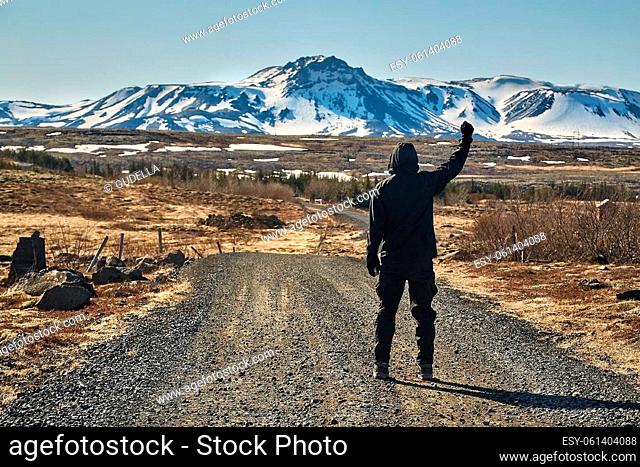 walking on gravel road throught Icelandic landscape, man raising hand in the air, feeling strong and triumphant