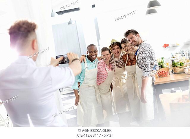 Chef teacher photographing students with camera phone in cooking class kitchen