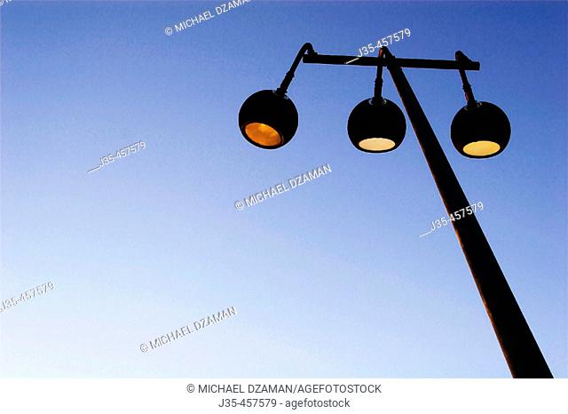 Three street lamps on pole at dusk against a clear blue sky
