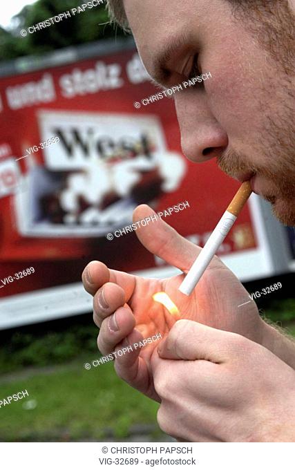 Man is lighting a cigarette in front of a cigarette promotional poster (West ). - BONN, GERMANY, 30/05/2003