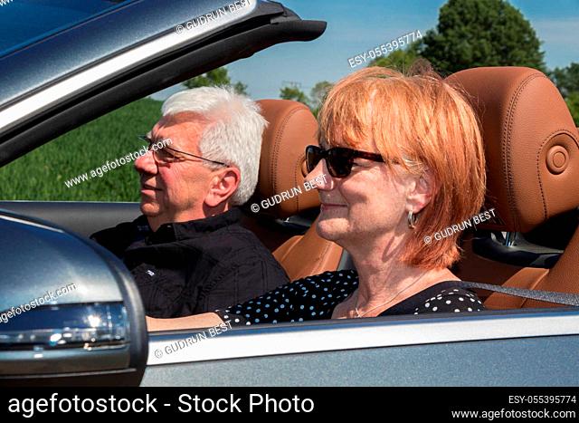 Older couple drives with a luxury convertible car on a sunny day