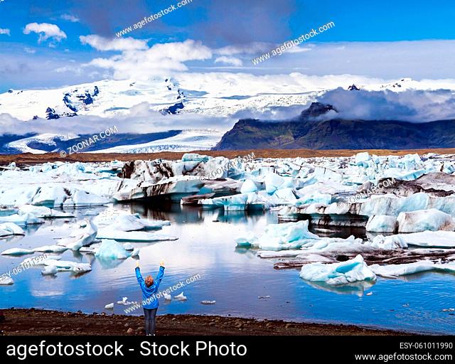 Enthusiastic woman tourist on the lagoon. Iceland. White and blue icebergs and ice floes reflected in the water. The concept of extreme