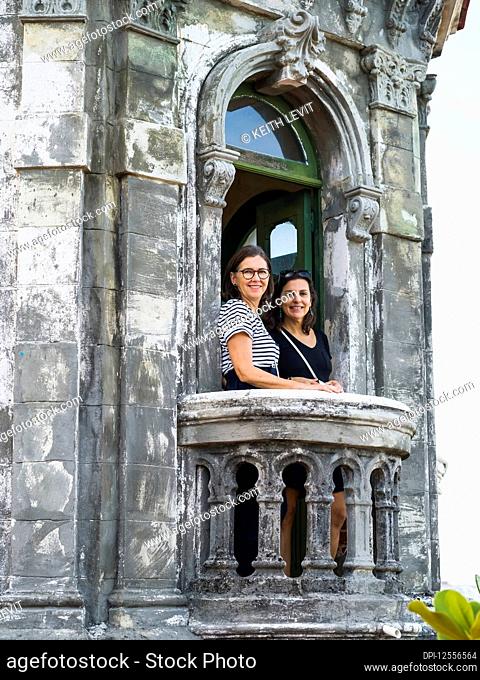 Two women stand on the balcony of an old building looking at the camera; Havana, Cuba