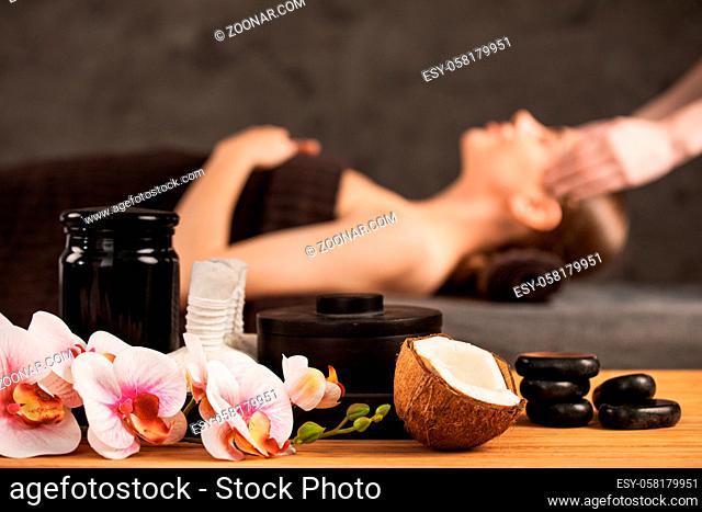 Beautiful woman getting head massage in spa orchid flowers coconut and stones