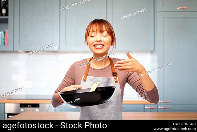 happy woman in apron with frying pan smelling food